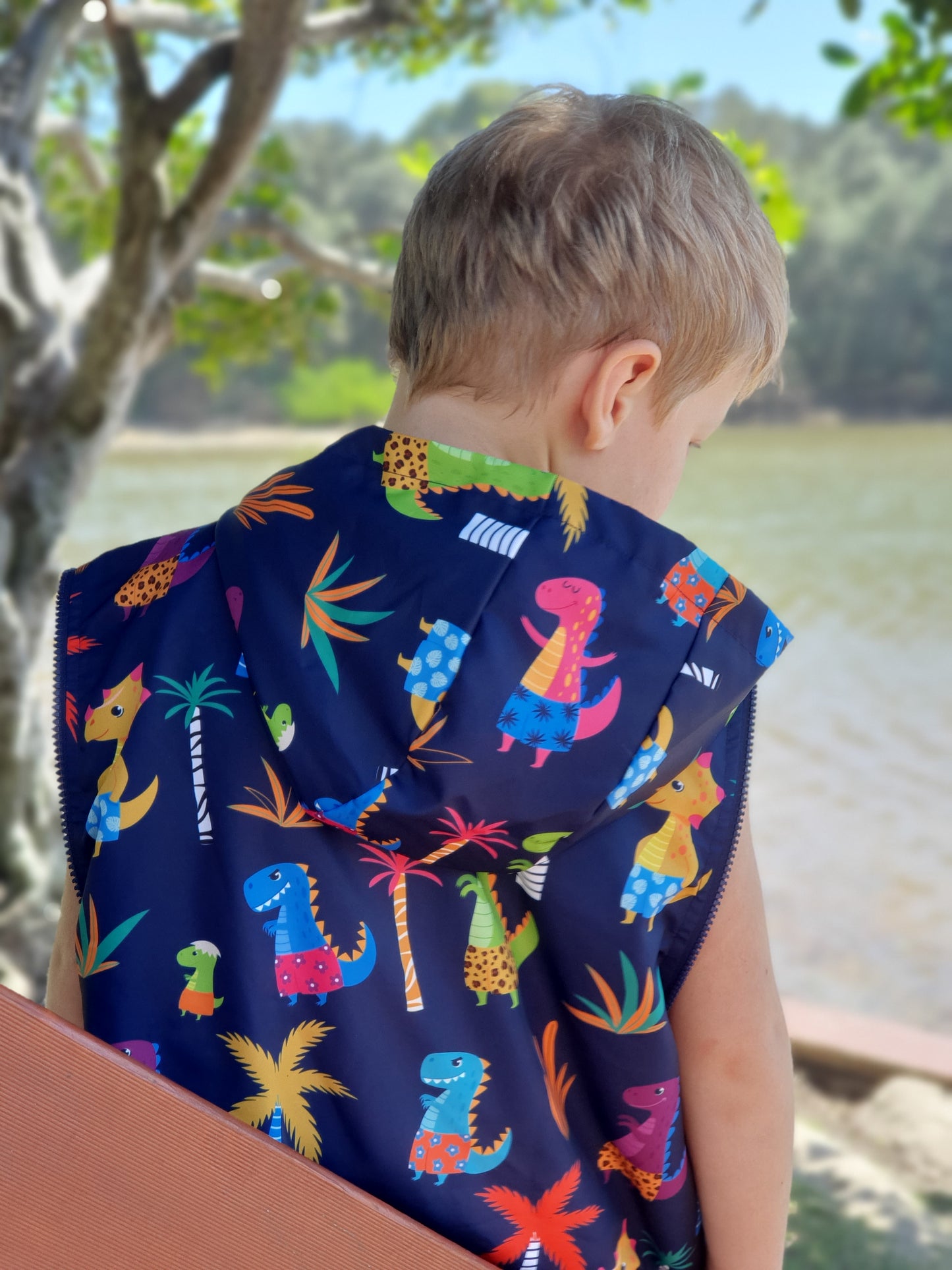 Dinosaur print swim parka. Boy is standing at beach wearing a swim parka. Schmik swim parka has removable sleeves and dinosaur print. 