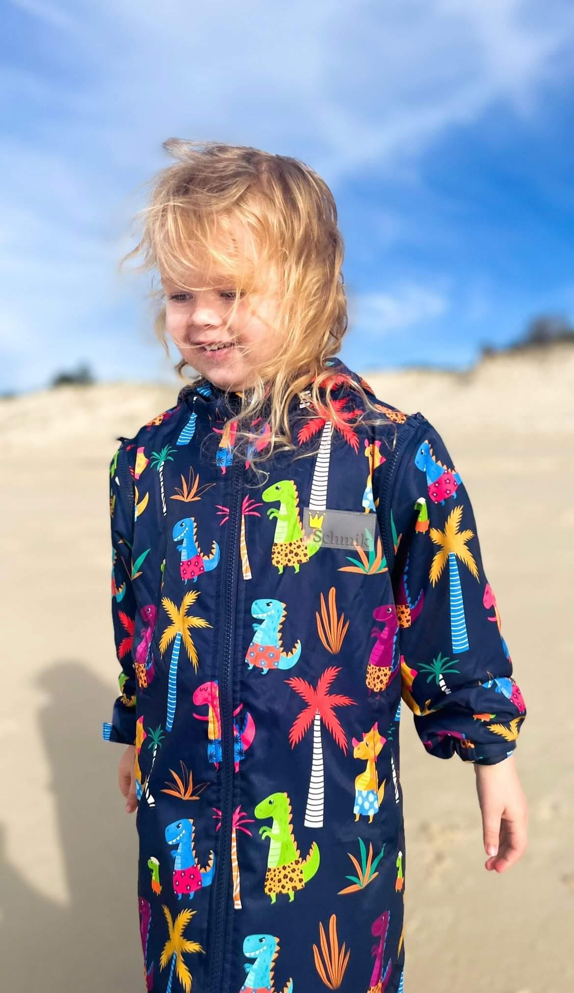 Toddler wearing dinosaur swim parka in navy print. Schmik swim parka can be worn after swimming lessons and nippers instead of a towel. Schmik swim parkas can be bought on Amazon.com