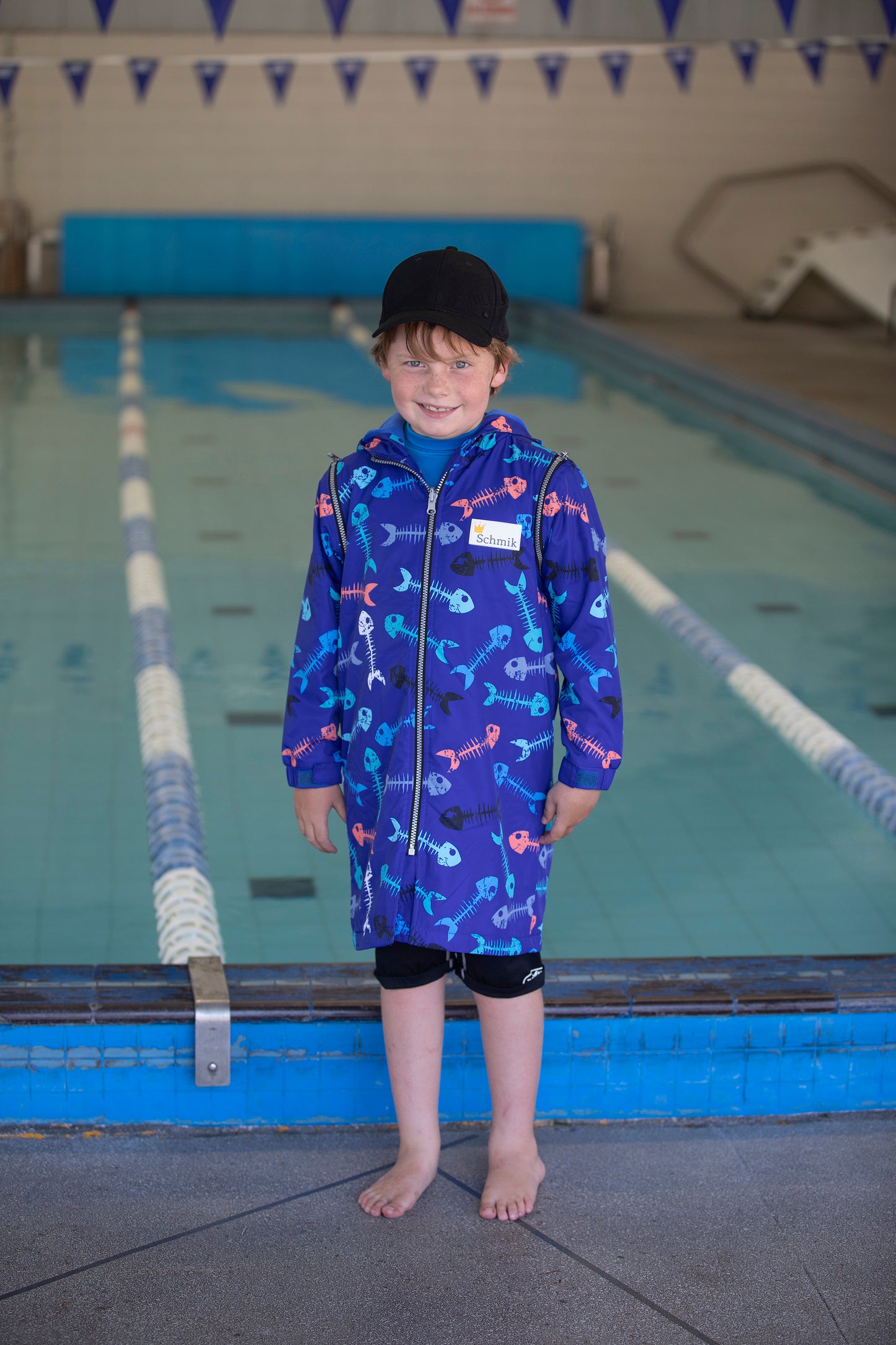 7 year old boy standing next to a pool wearing a schmik swim parka in a blue fishbone print.