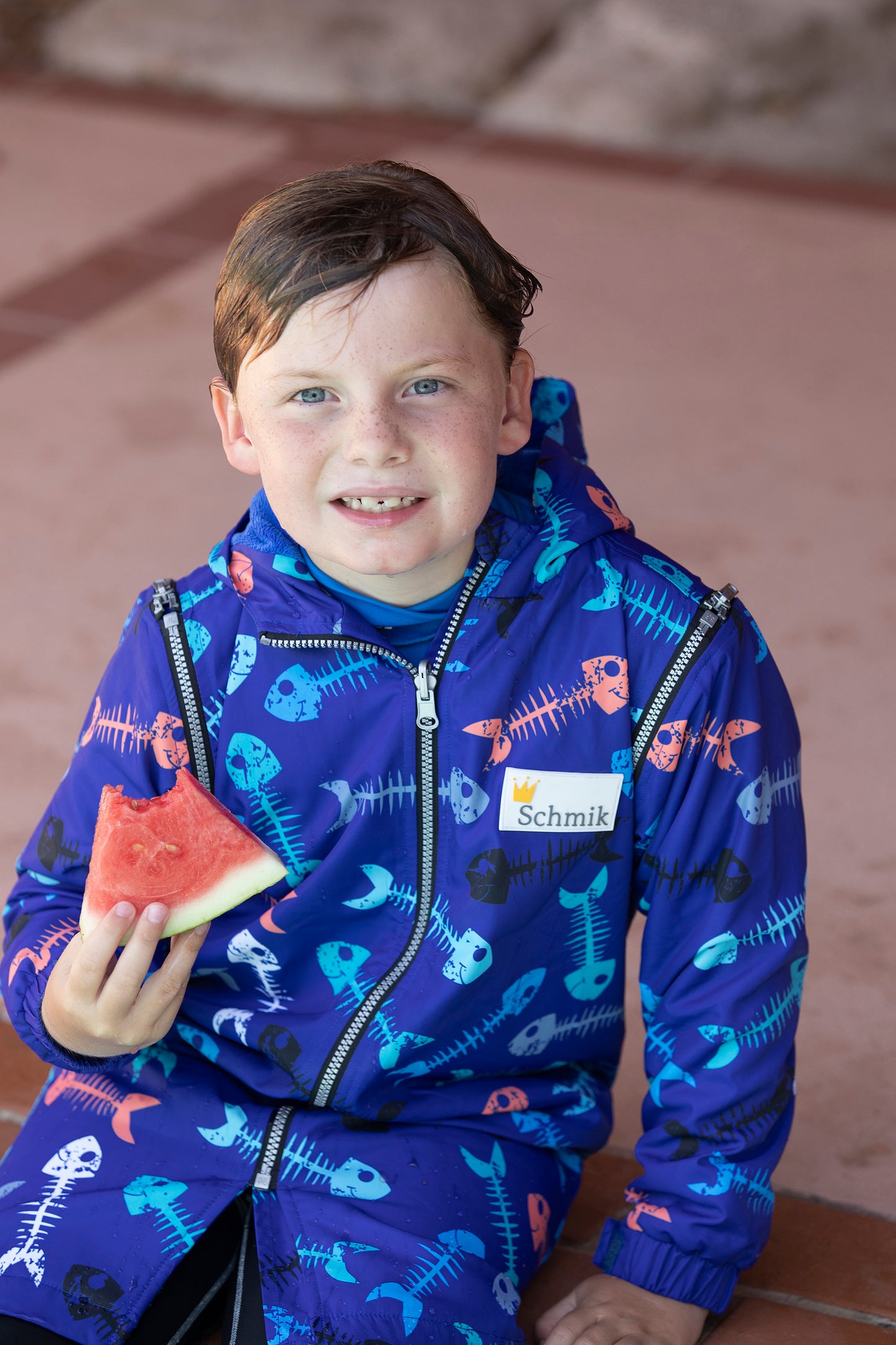 Boy wearing blue fishbone swim parka in size 8 . Boy is sitting on pool edge. Swim parka is showerproof and ideal for pools and beach.