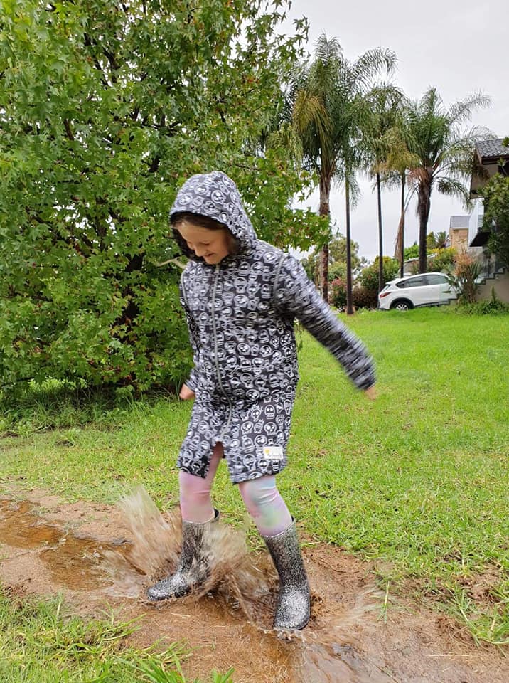 Girl jumping in muddy puddles wearing a schmik swim parka with skull print. Schmik swim parka has a showerproof outer, ideal for walking in the rain.