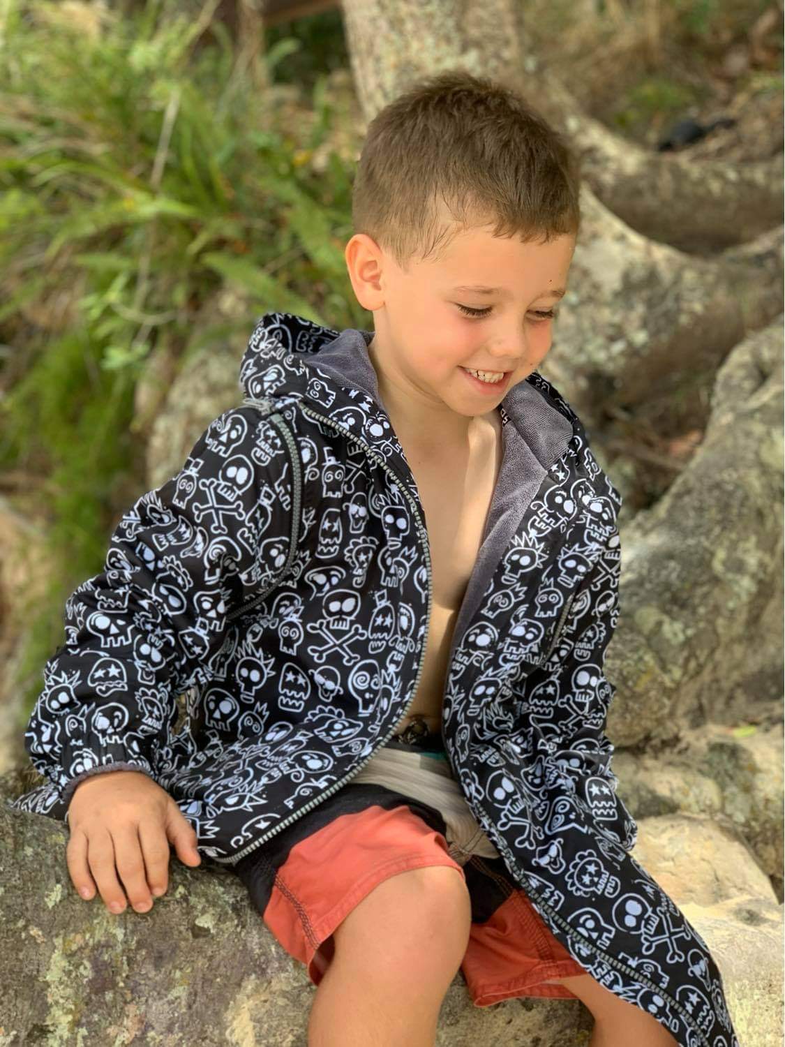 Boy sitting on tree at the beach wearing skull and bones swim parka.
