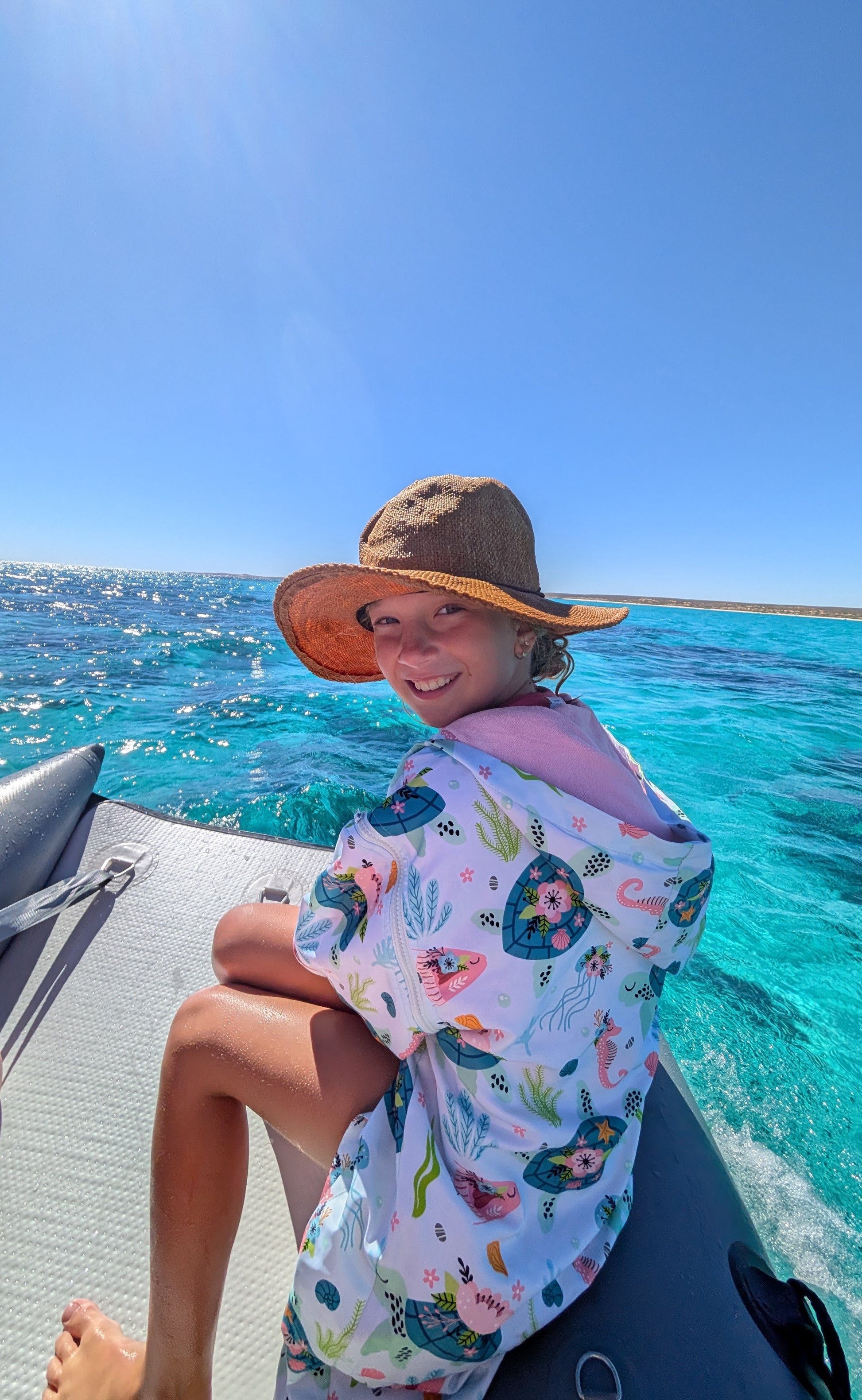 Sea Haven swim parka on girl sitting on boat in the turquoise sea in the ningaloo reef. 