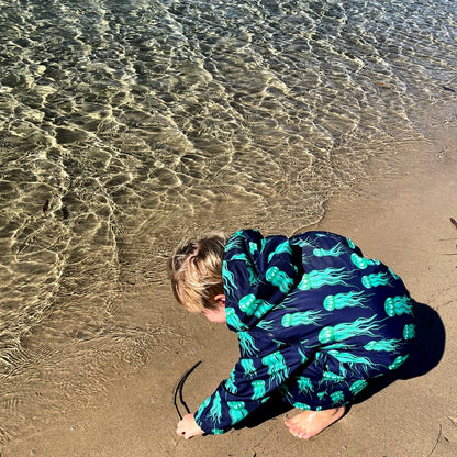 Child playing on the beach wearing a schmik swim parka. Swim parka has a jelly fish print and is perfect for the beach and swimming.