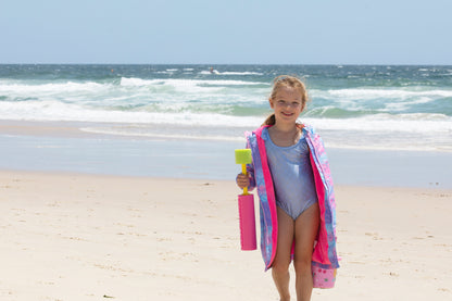 Child standing on the beach wearing pink mermaid swim parka holding water gun toy. 