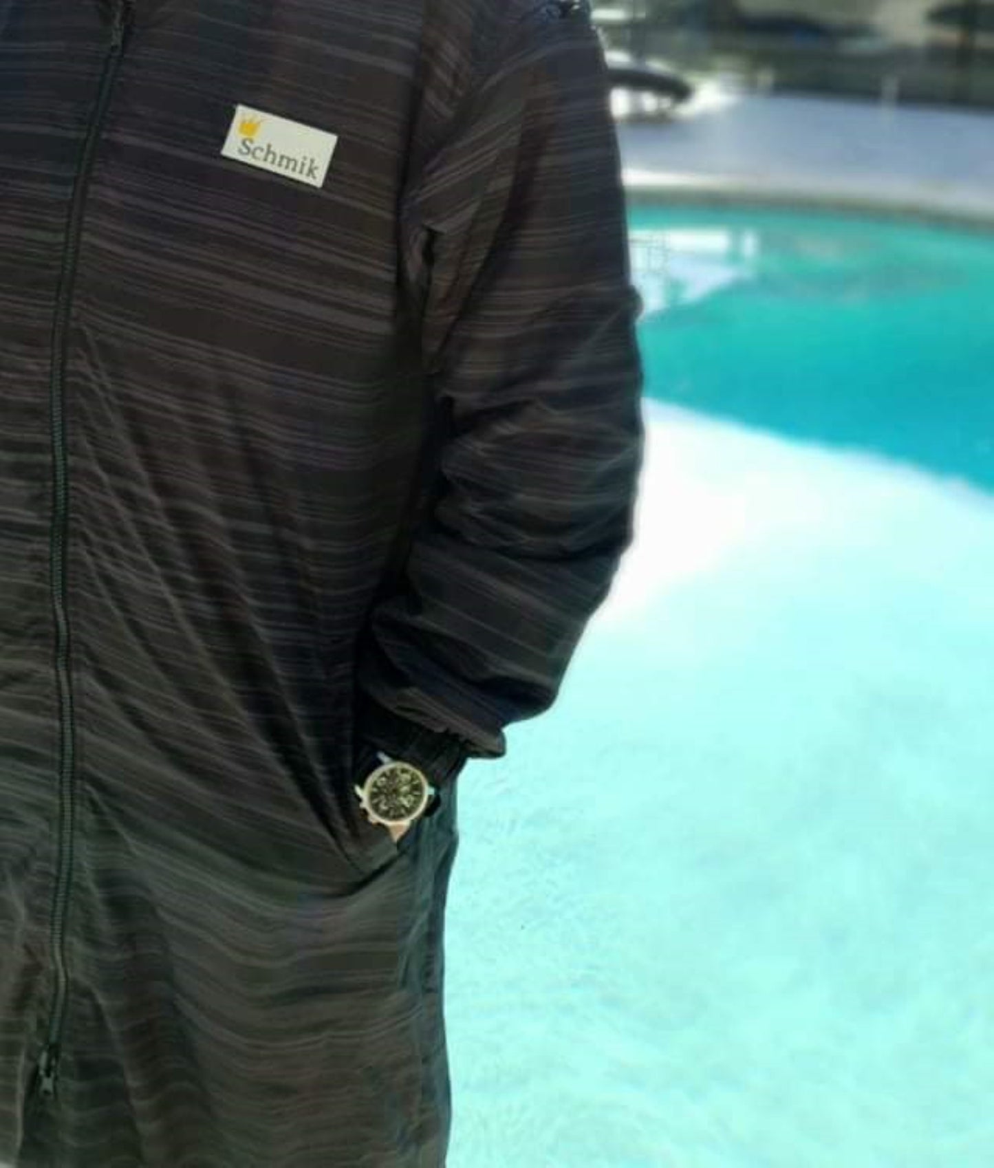Adult wearing a black print Schmik swim parka. Adult is standing in front of a swimming pool. 