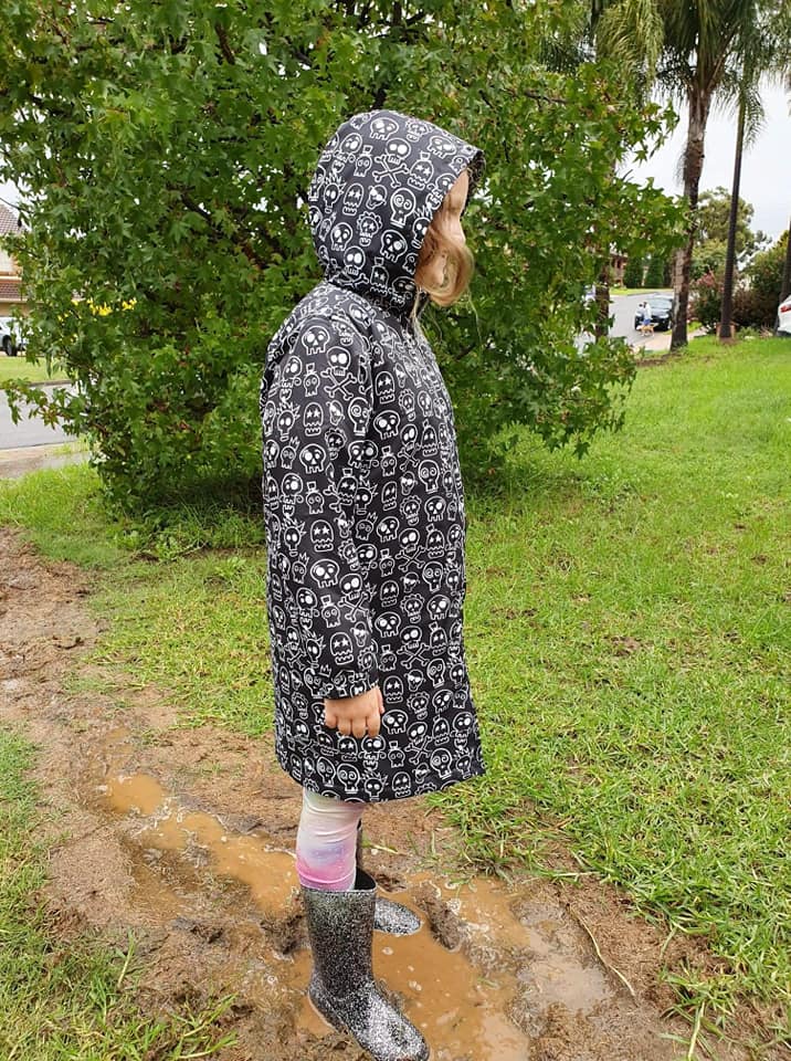 Girl standing in a muddy puddle wearing gumboots and a schmik swim parka in skull and bones print.